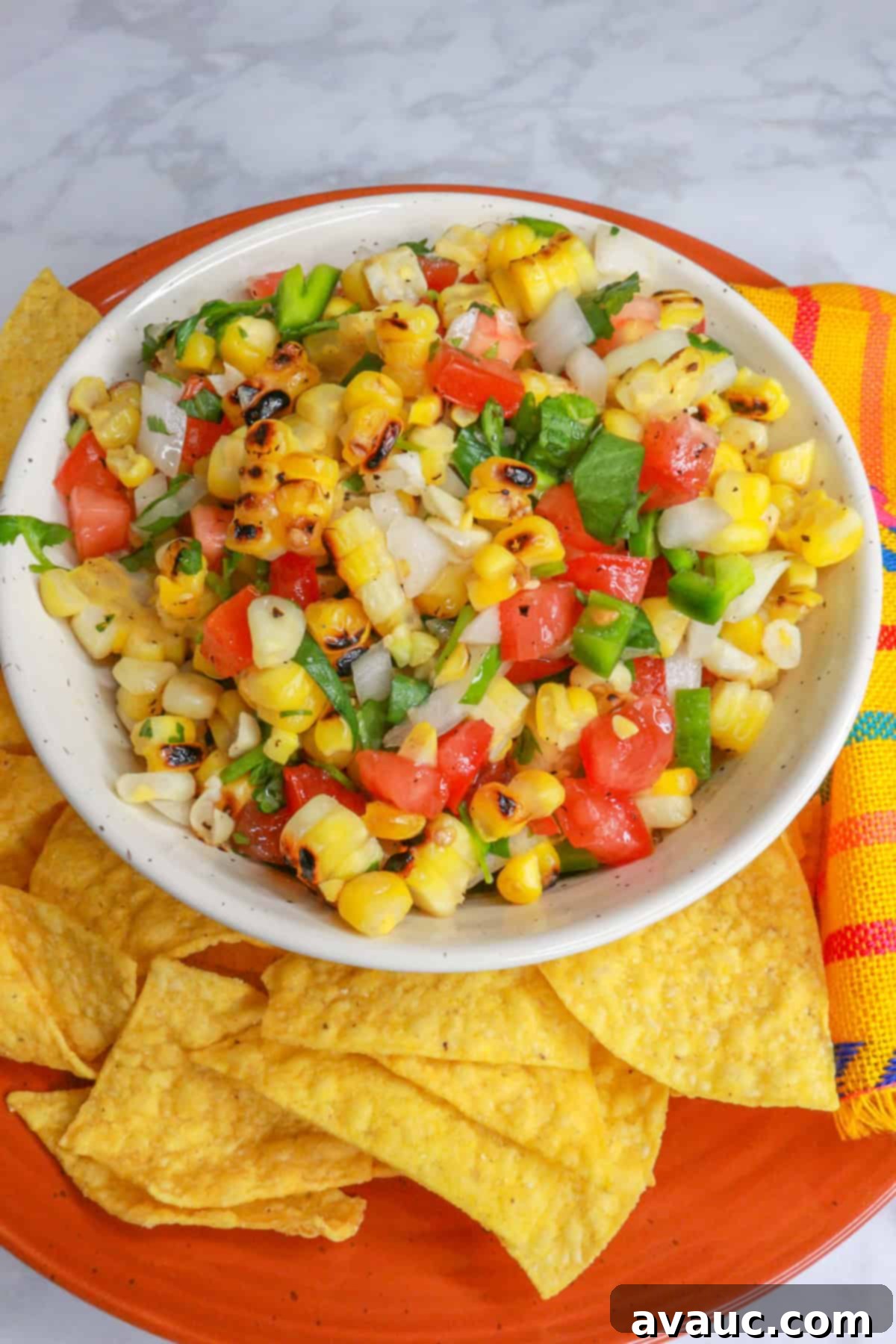A beautiful close-up of the roasted corn pico de gallo, with a few tortilla chips in the background, ready for dipping.