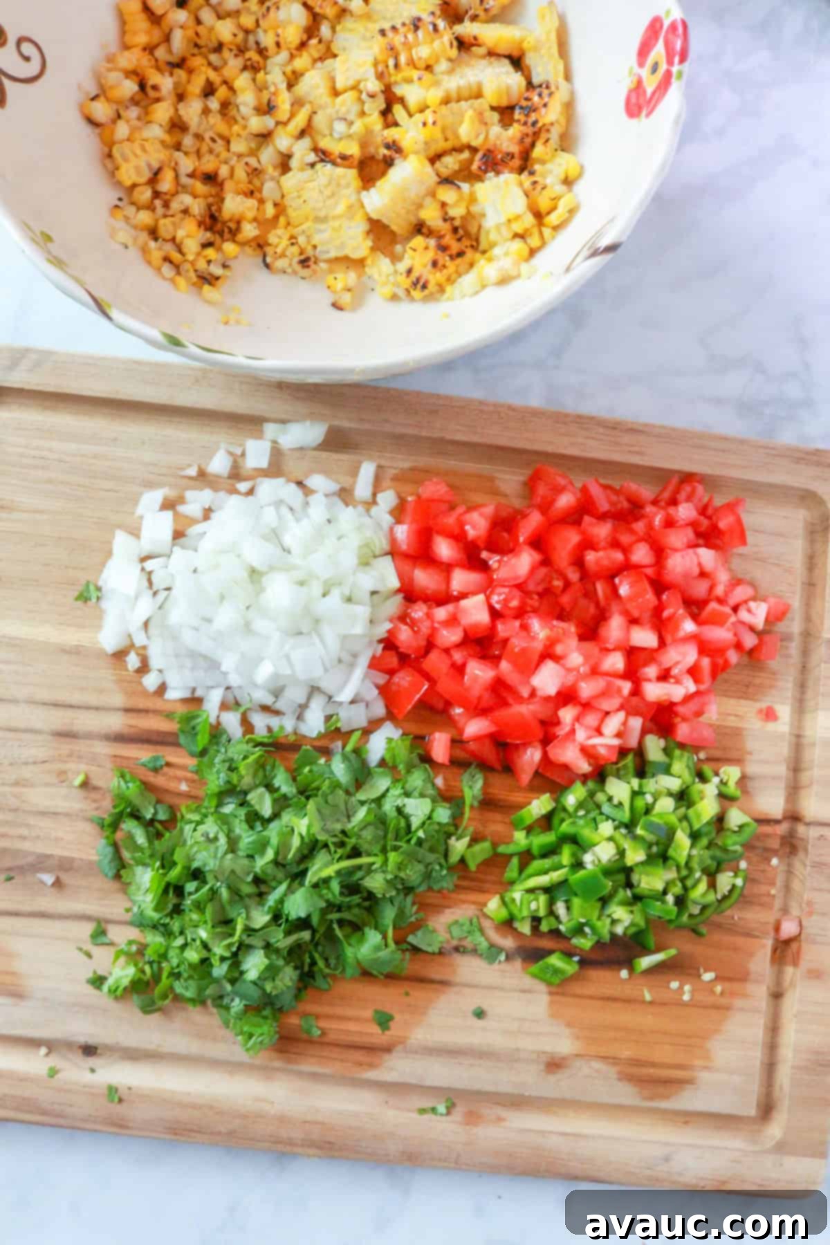 A cutting board with uniformly diced cilantro, onion, tomatoes, and jalapeños, ready to be mixed with the roasted corn.