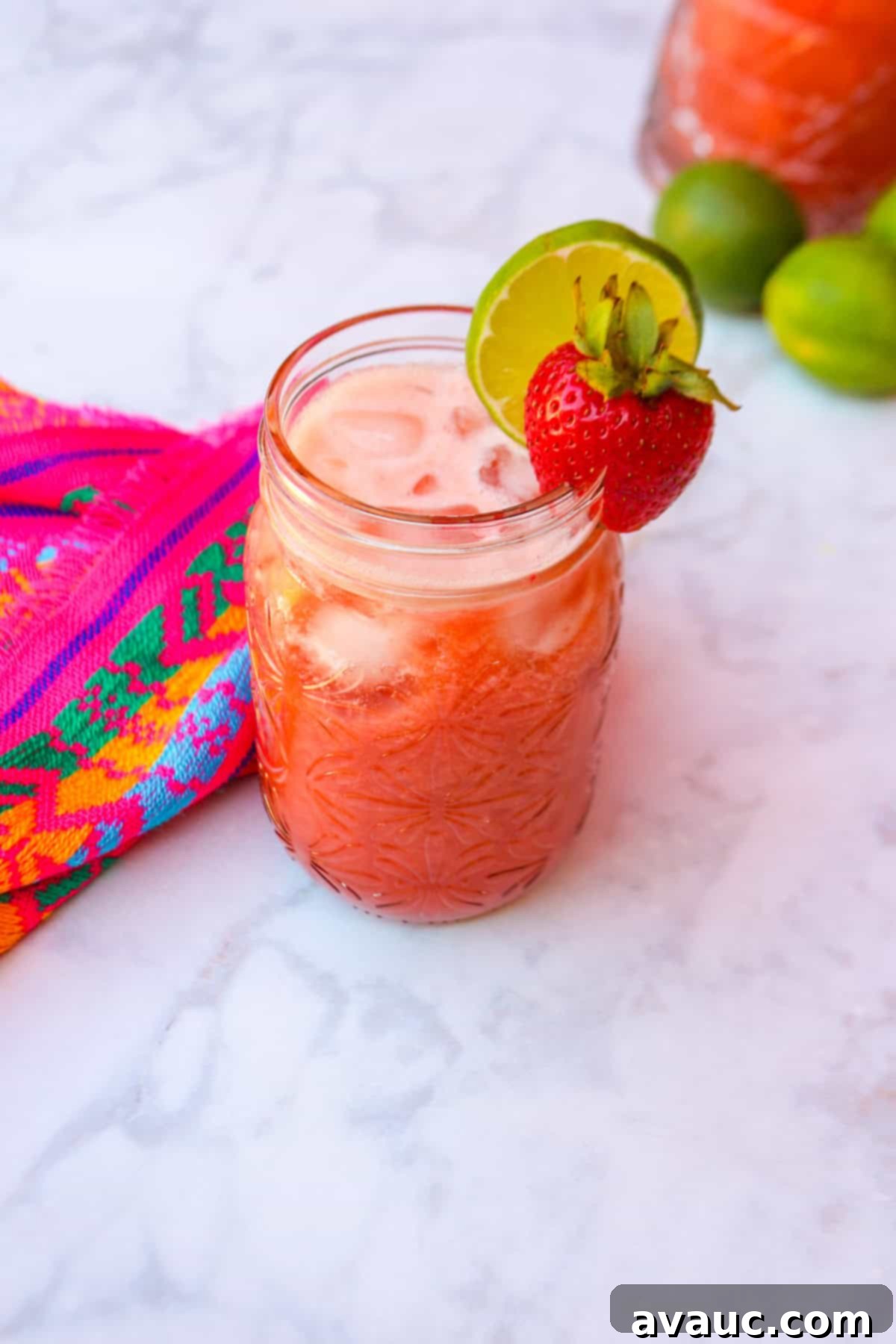 Strawberry Limeade 2 Limonada de fresa in a glass, garnished with a strawberry and slice of lime, sitting on a wooden table outdoors