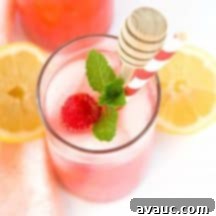 A glass of pink raspberry lemonade with fresh raspberries and lemon slices.