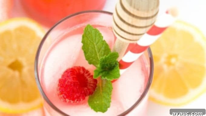 Two glasses of raspberry lemonade with fresh mint and berries, next to a pitcher.