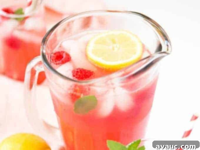 A close-up of raspberry lemonade in a glass, with a honey dipper stirrer.
