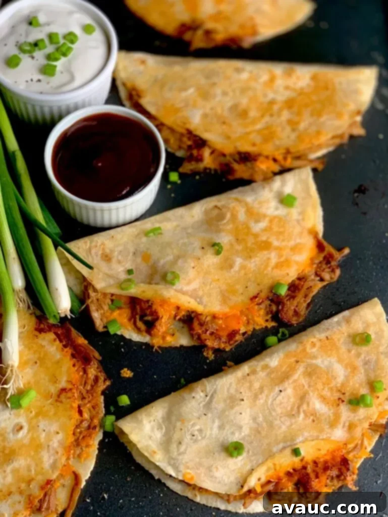 Three crispy looking tortillas with a brown pulled pork sticking out and yellow melted cheese on a black griddle next to a small bowl of BBQ sauce and green onions.
