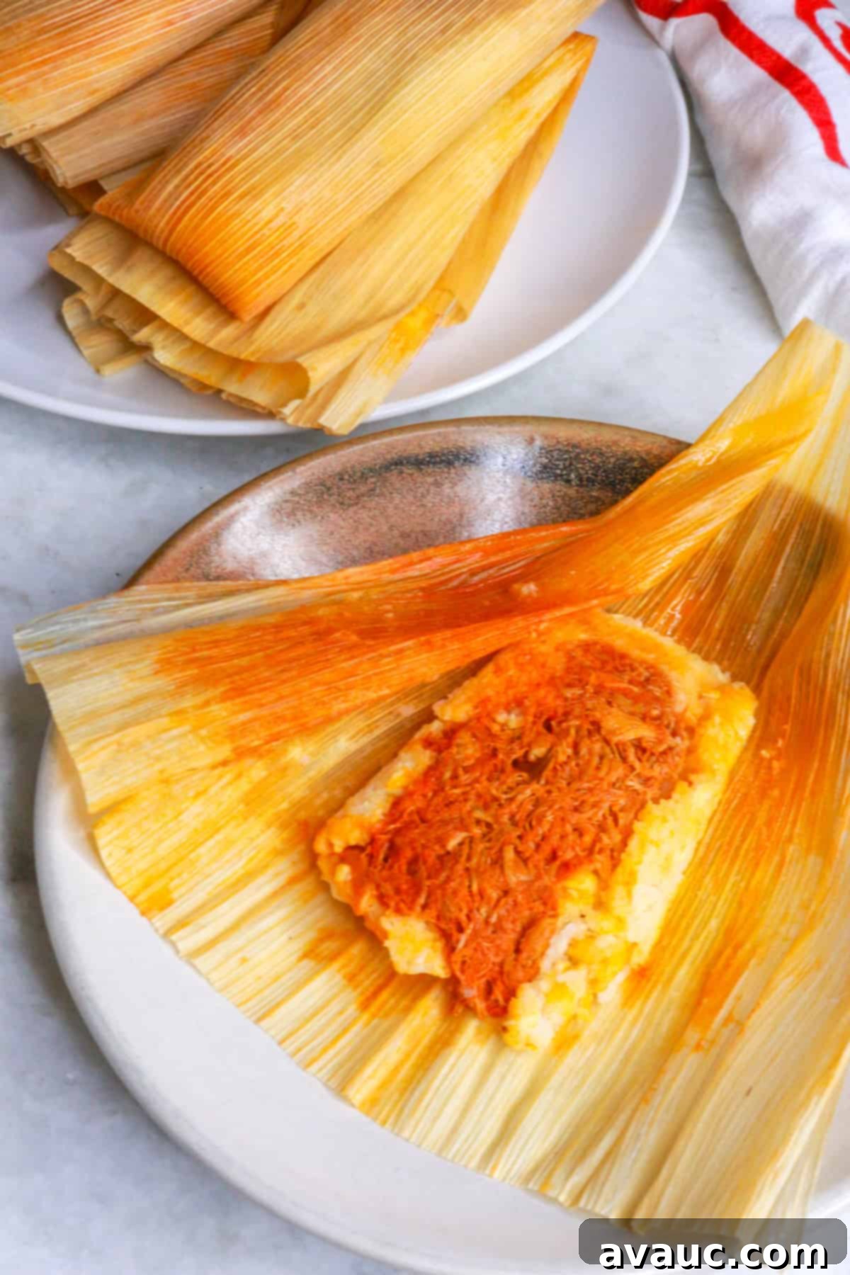 Red Chile Pork Tamales 17 Mexican tamales rojos on a plate and one tamal unwrapped on a brown plate