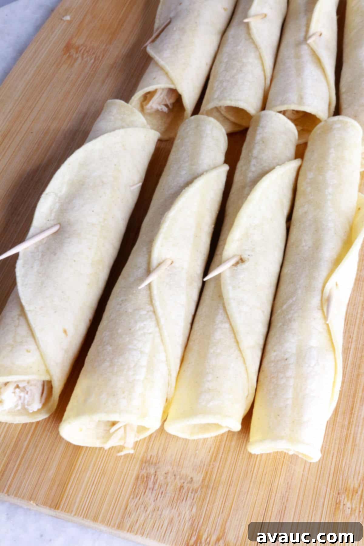 Crispy Rolled Chicken Tacos 6 Rolled flautas on a wooden cutting board waiting to be fried