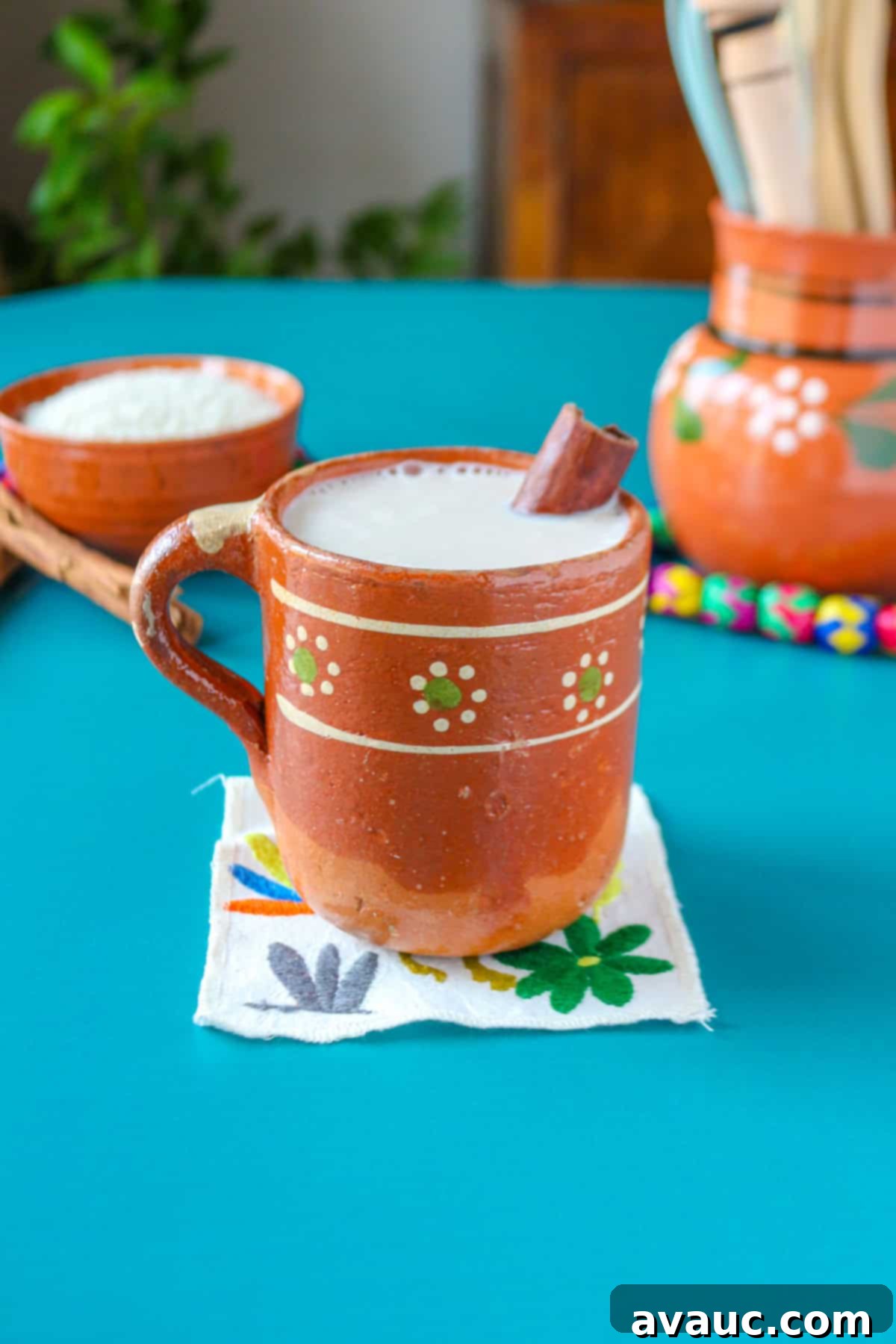 Creamy Rice Atole Dairy-Free Friendly 2 Rice atole in a Mexican mug garnished with a cinnamon stick with a bowl of rice behind it and a pitcher with utensils