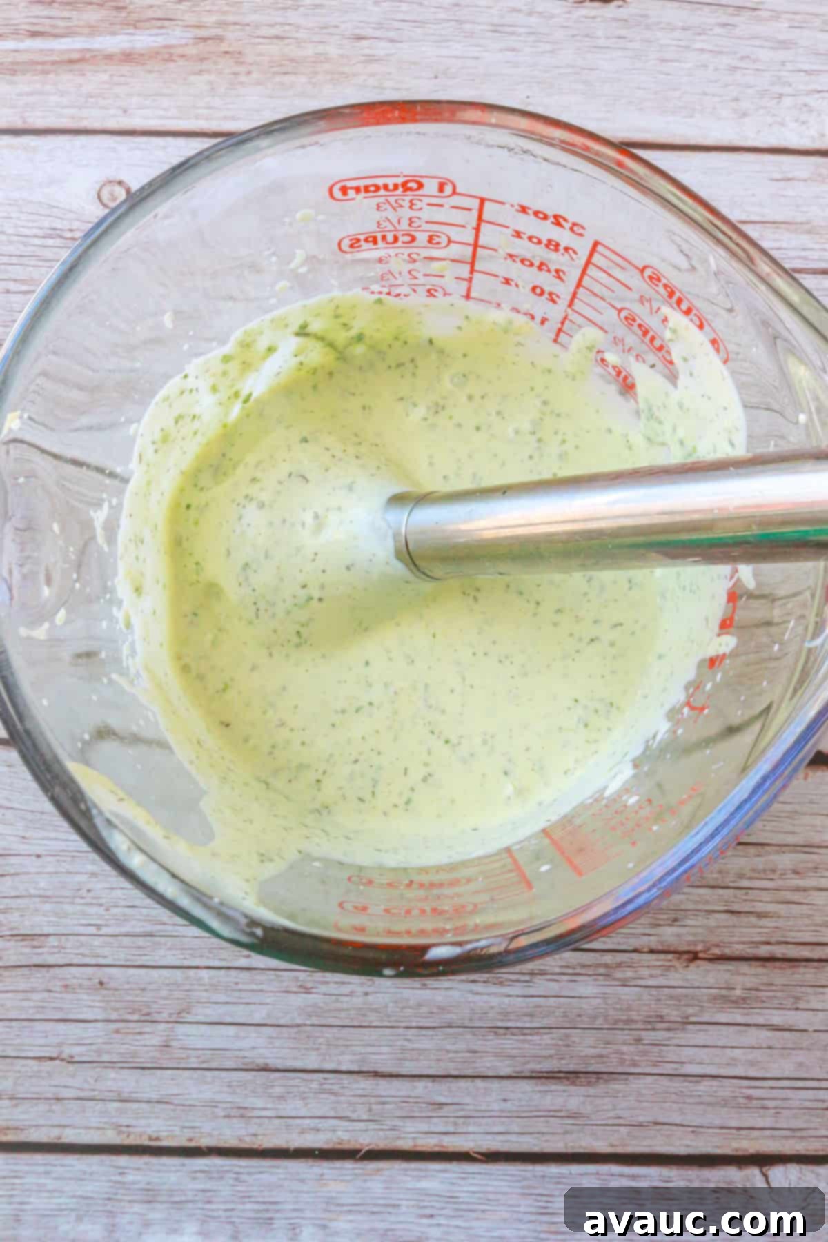 Vegan Creamy Serrano Ranch 6 A smooth, green serrano ranch dressing being blended in a glass measuring cup with an immersion blender, showcasing the creamiess.