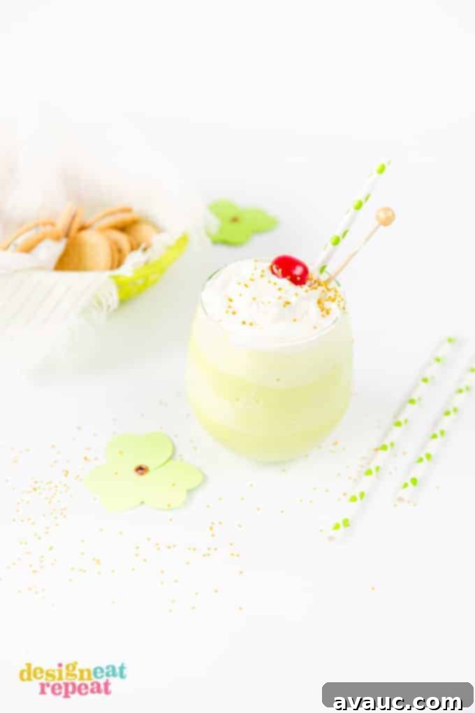 Mint Shamrock milkshake in glass cup topped with whipped cream, a cherry, and gold sprinkles.