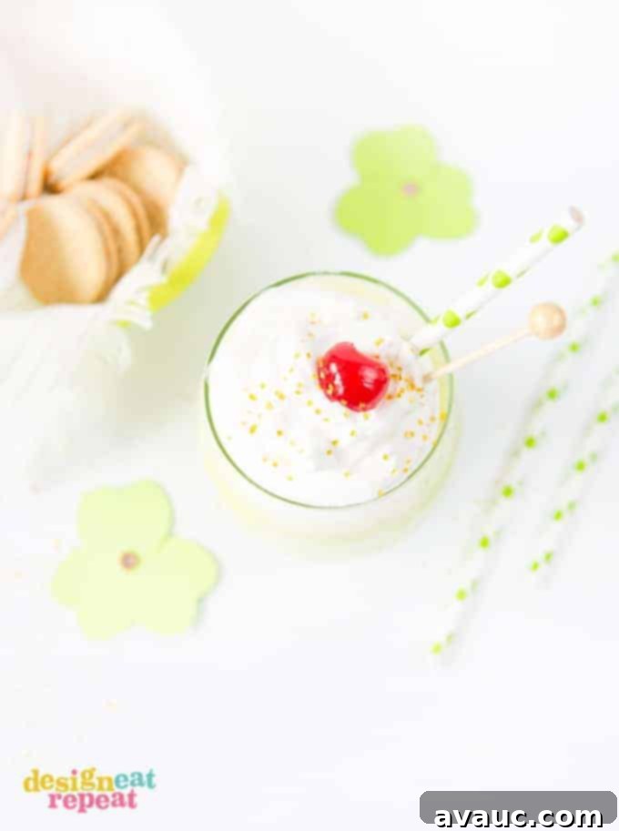 Mint Shamrock milkshake in glass cup topped with whipped cream, a cherry, and gold sprinkles.