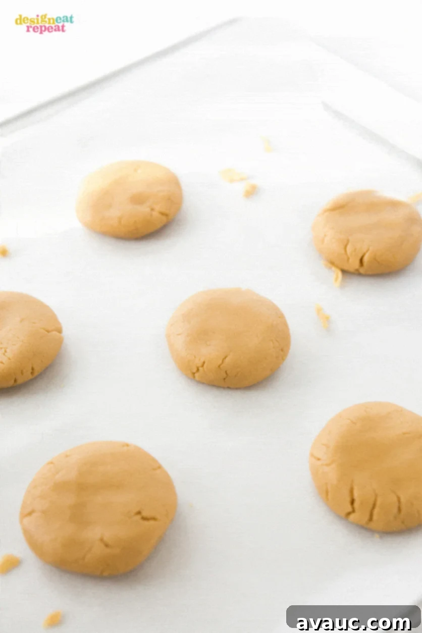 Peanut butter cookie dough balls being shaped and flattened on baking sheet.