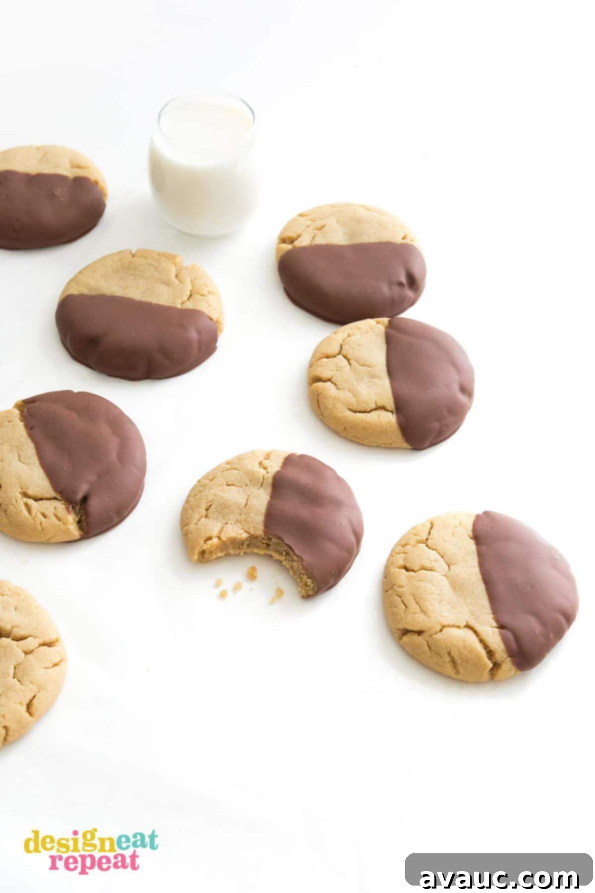 Table of peanut butter cookies dipped in chocolate with bite and glass of milk.