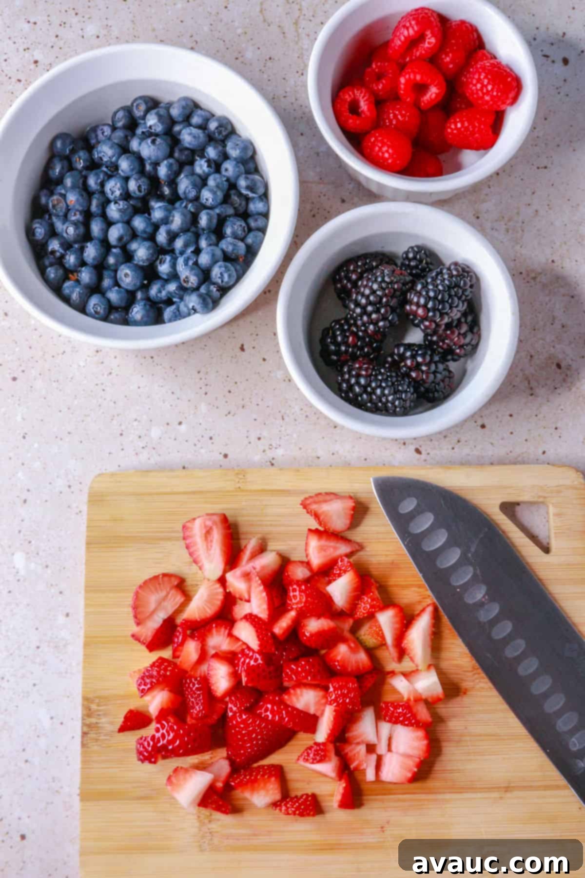 Luscious Dairy-Free Berries and Cream 6 A bowl filled with a colorful assortment of fresh mixed berries, including strawberries cut into quarters, alongside whole blueberries, raspberries, and blackberries, all washed and prepped.