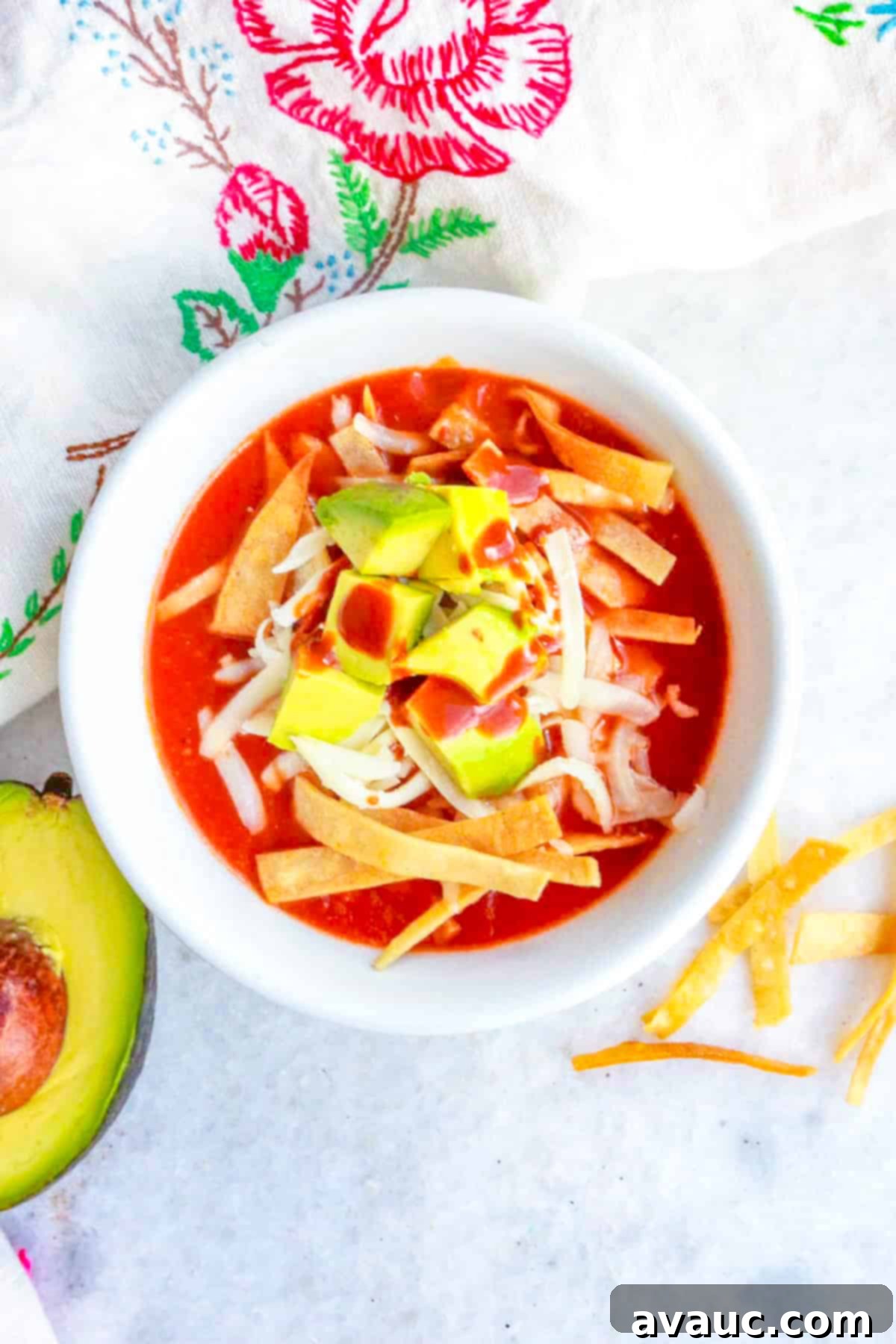 Aztec Tortilla Soup 2 A bowl of Sopa de Tortilla Azteca, a classic Mexican tortilla soup, garnished with crispy tortilla strips, fresh avocado, shredded Mexican cheese, and a drizzle of hot sauce, viewed from the top.