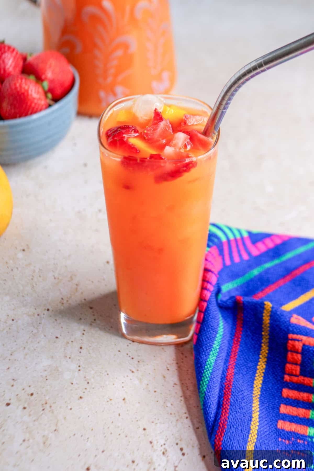 Glass of strawberry mango Agua Fresca garnished with pieces of fruit and a metal straw