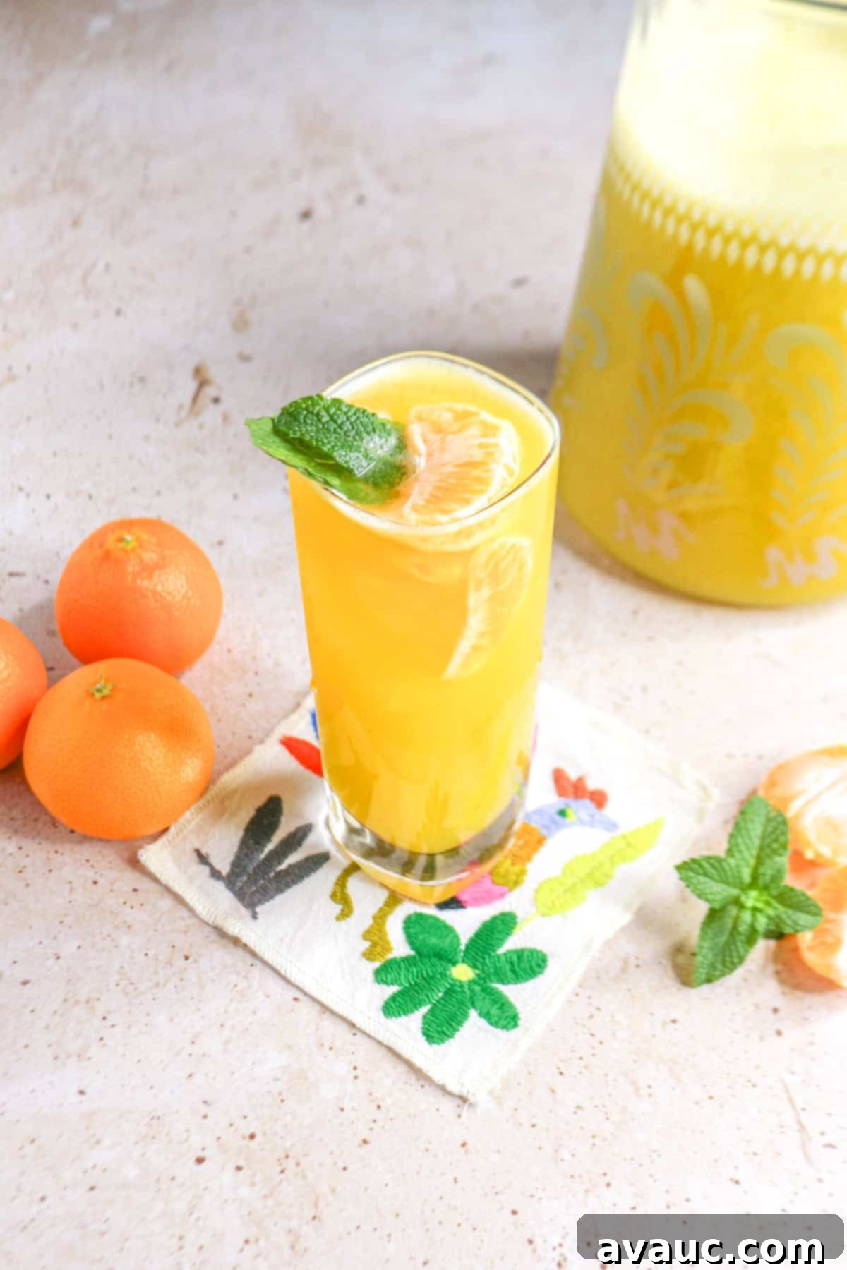 Refreshing Mandarin Mint Agua Fresca 2 Glass of mandarin Agua Fresca with mint on a coaster with a pitcher of the Agua Fresca behind it