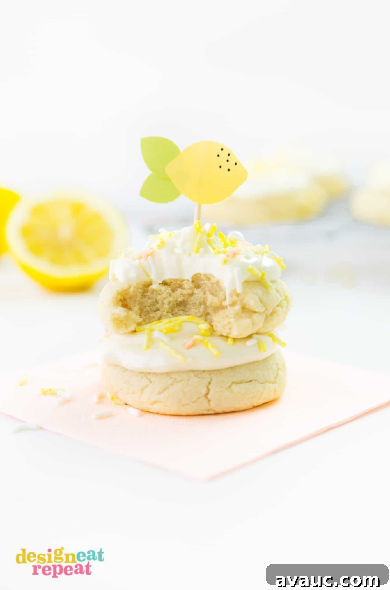 Welcome summertime with these delicious Soft & Thick Lemon Sugar Cookies. They are easy to make and are infused with a refreshing, light lemon flavor! Get the recipe at DesignEatRepeat.com Stack of thick lemon sugar cookies with frosting, yellow sprinkles, and paper lemon toothpick topper on top, ready for summer enjoyment.