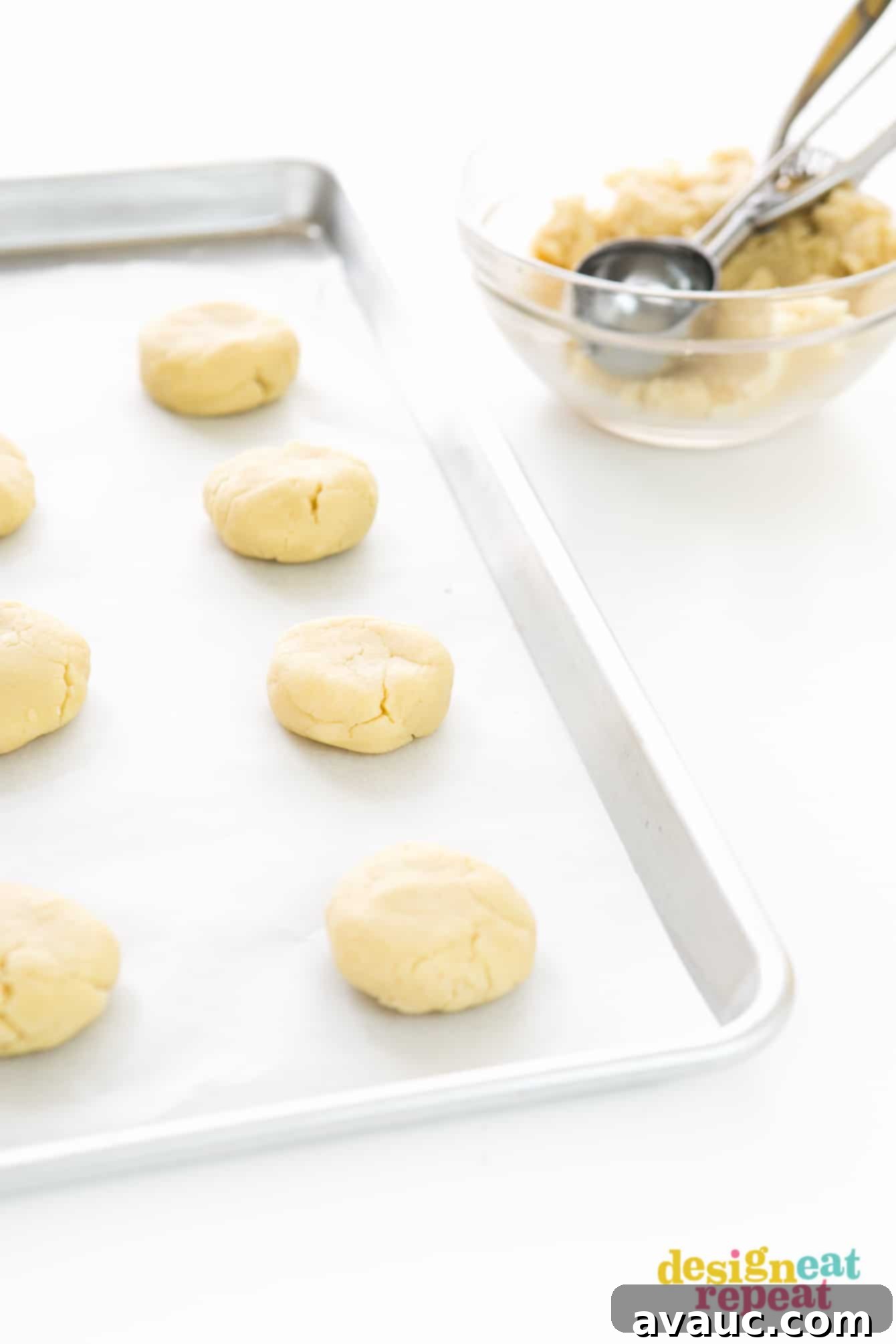 Luscious Lemon Cloud Cookies 4 Tray of raw thick lemon sugar cookie dough being scooped into balls with a metal scoop, showing the perfect size before baking.