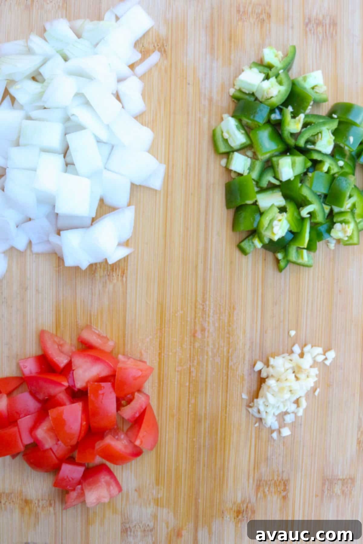 Chopped onions, jalapeños, tomatoes and garlic neatly arranged on a wooden cutting board