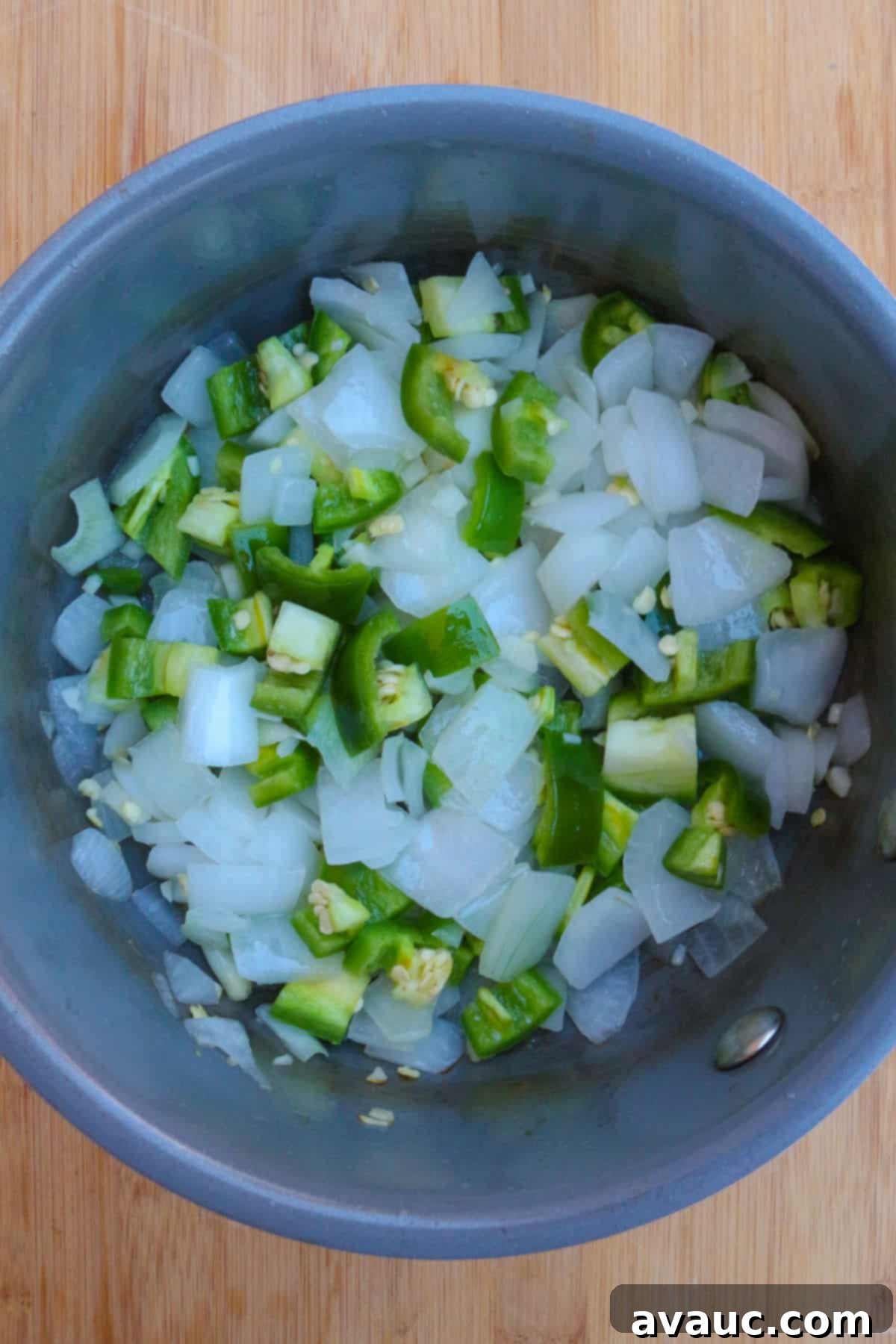 Sautéed chopped onions and jalapeños gently cooking in a small pot on the stovetop