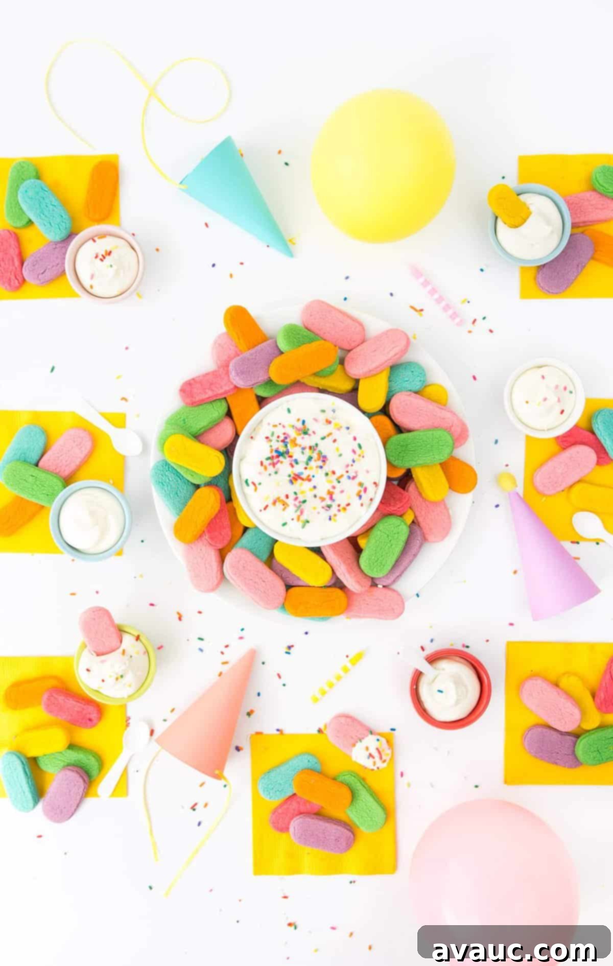 Overhead photo of party table with plate of rainbow sugar cookies on yellow napkins, balloons, and paper party hats.