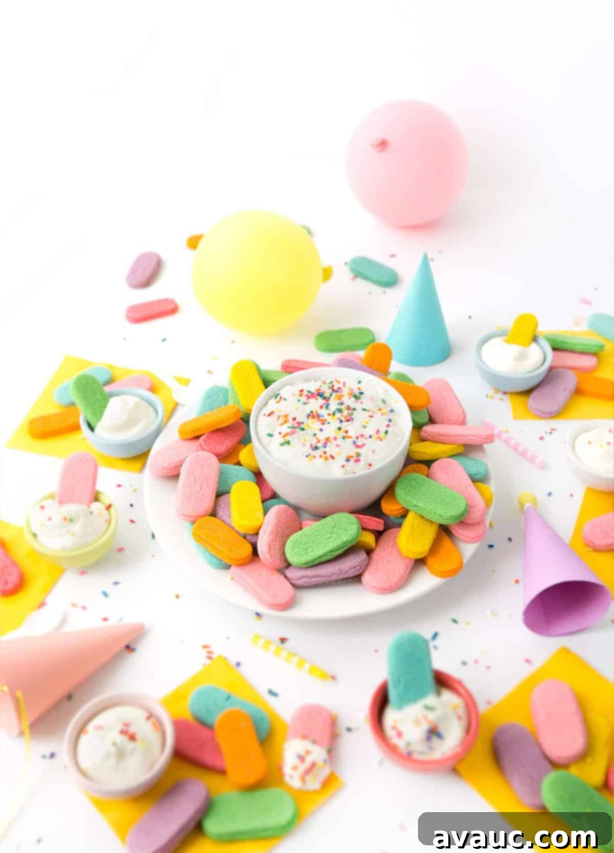 Plate of rainbow sprinkle sugar cookies with a bowl of cream cheese frosting in a party scene.