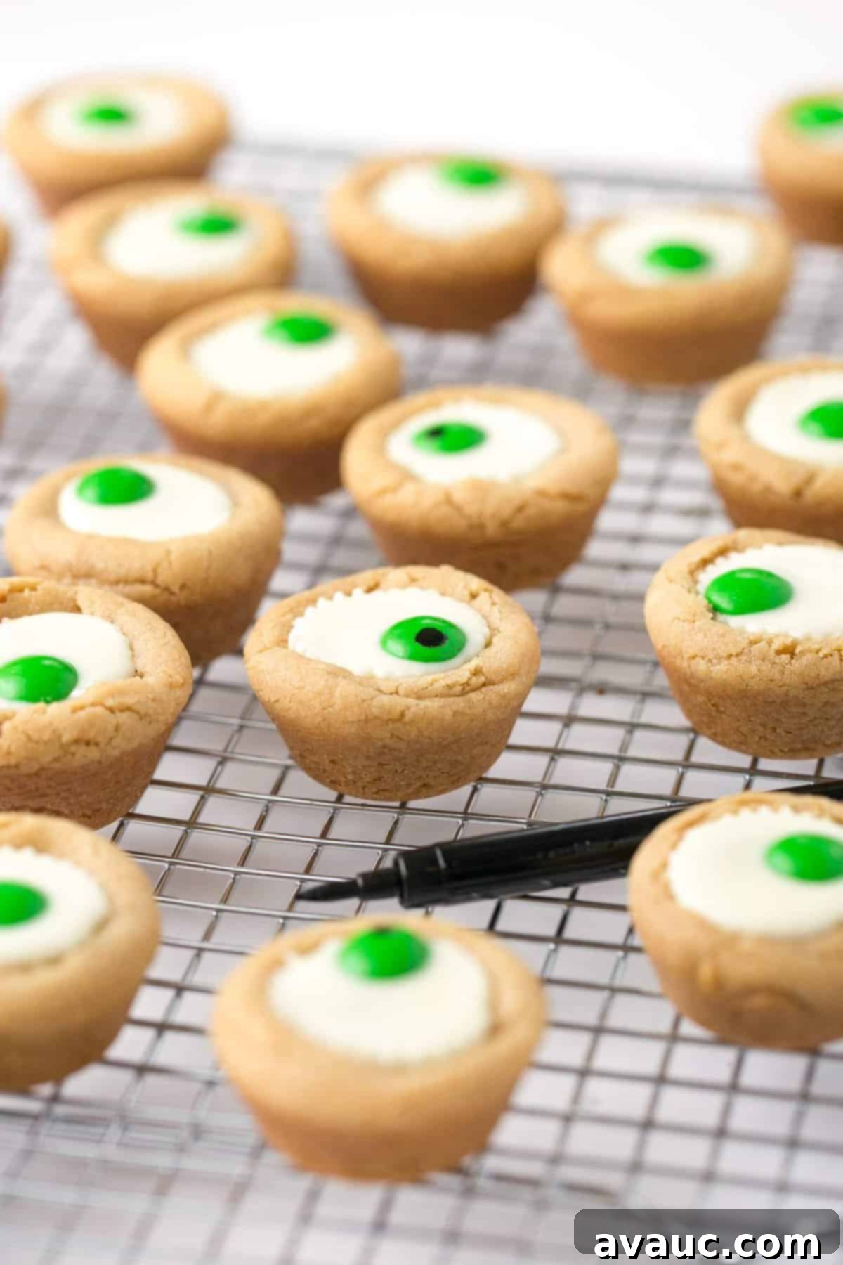 Spooktacular Peanut Butter Cup Eyeballs 9 Mini white peanut butter cup cookies on wire cooling rack with black food pen.