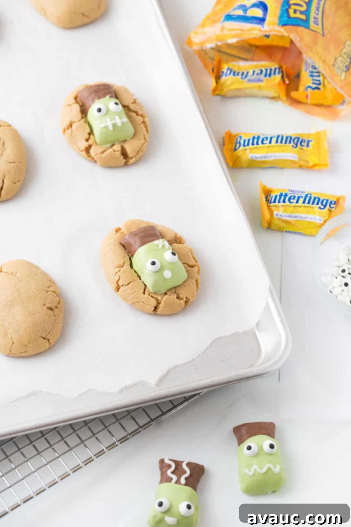 Peanut butter cookies on baking tray topped with decorated Frankenstein Butterfinger candy bars.