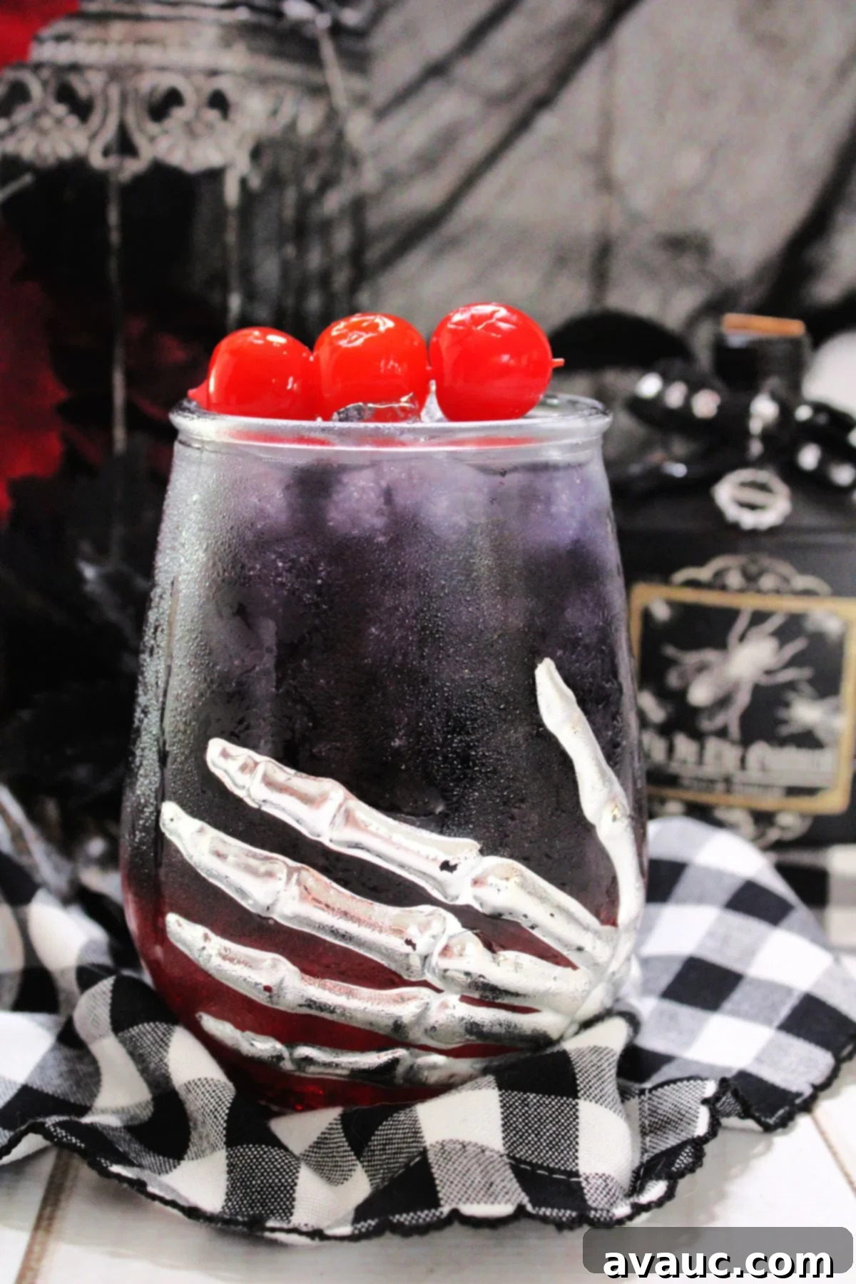 A Halloween-themed glass filled with a stunning layered Black Widow cocktail, elegantly garnished with fresh cherries on top.