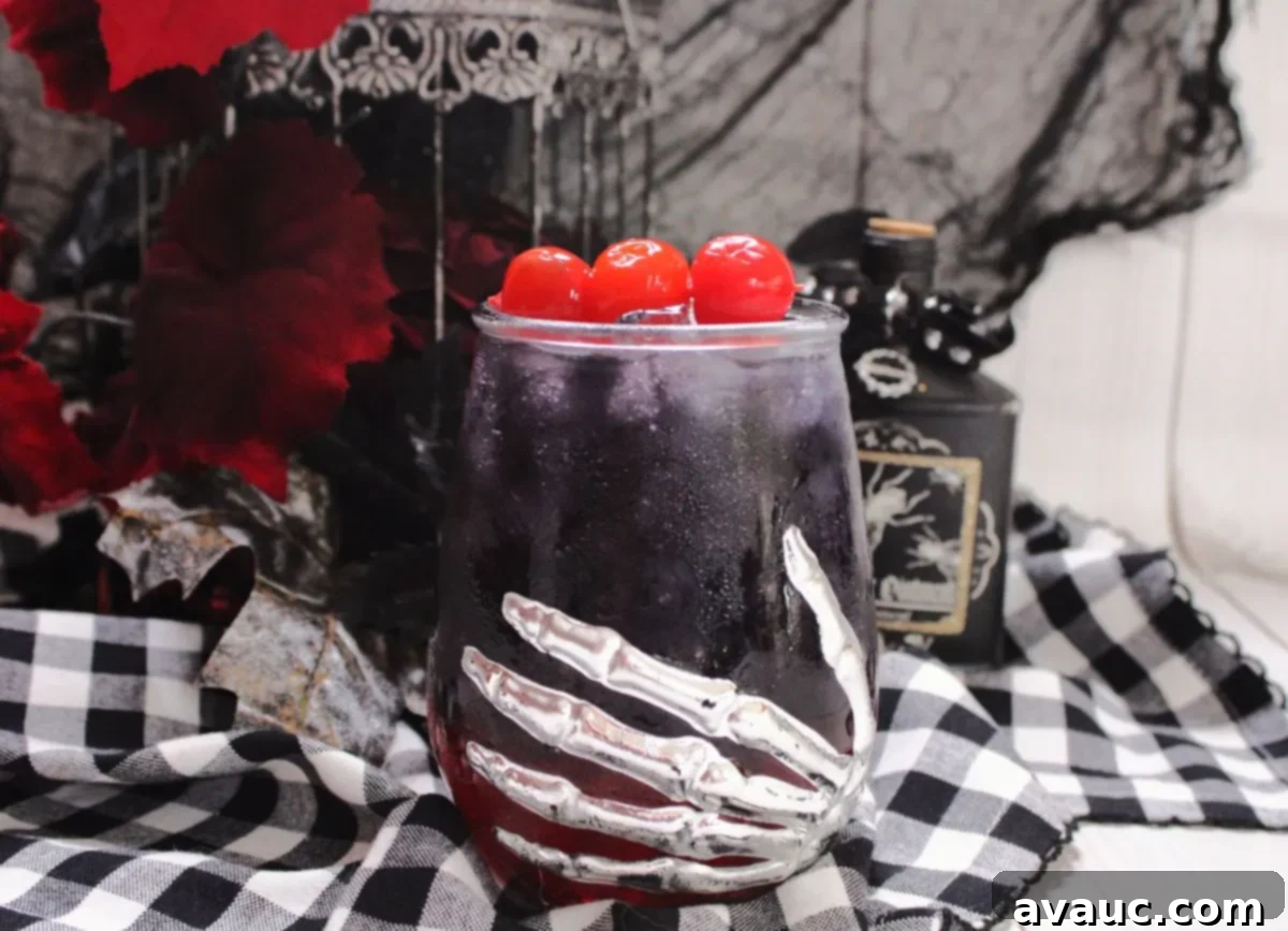 A Halloween-themed glass held by a skeleton hand, containing a two-toned Black Widow cocktail with a striking red and black layer.