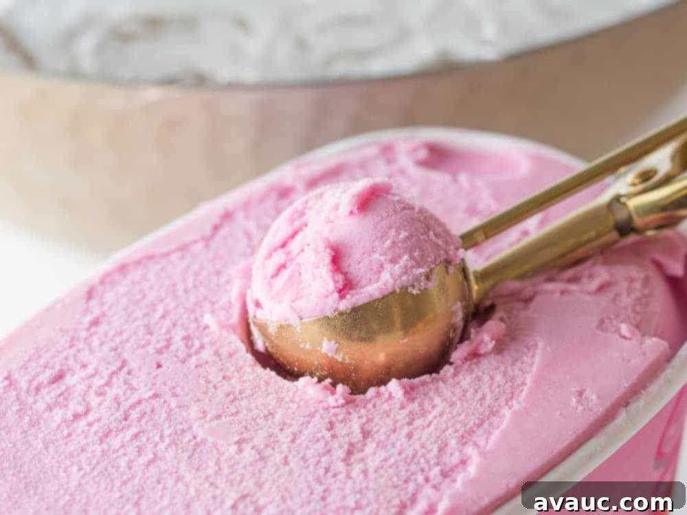 Scooping vibrant raspberry sherbet from a carton with a gold ice cream scoop into a jar.