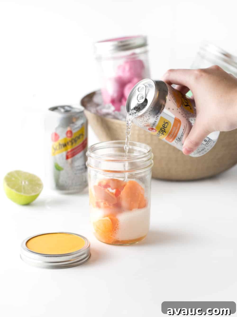 A hand pouring Schweppes Orange Sparkling Water into a glass with orange sherbet, creating a fizzy punch.