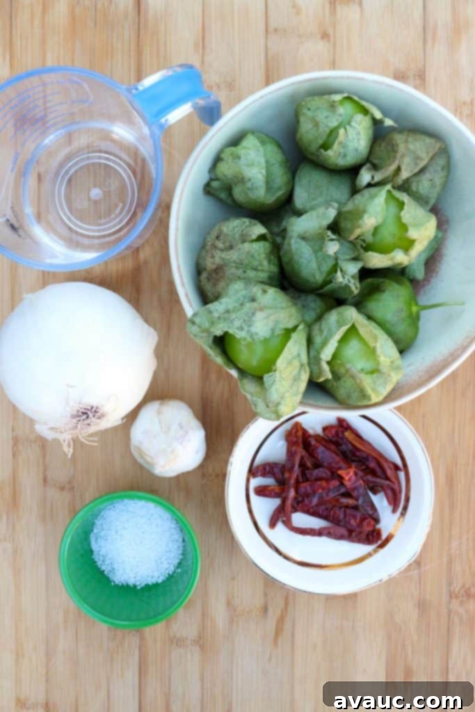 Tomatillos in a bowl, water in a measuring cup, chiles de arbol, salt, garlic and onion.