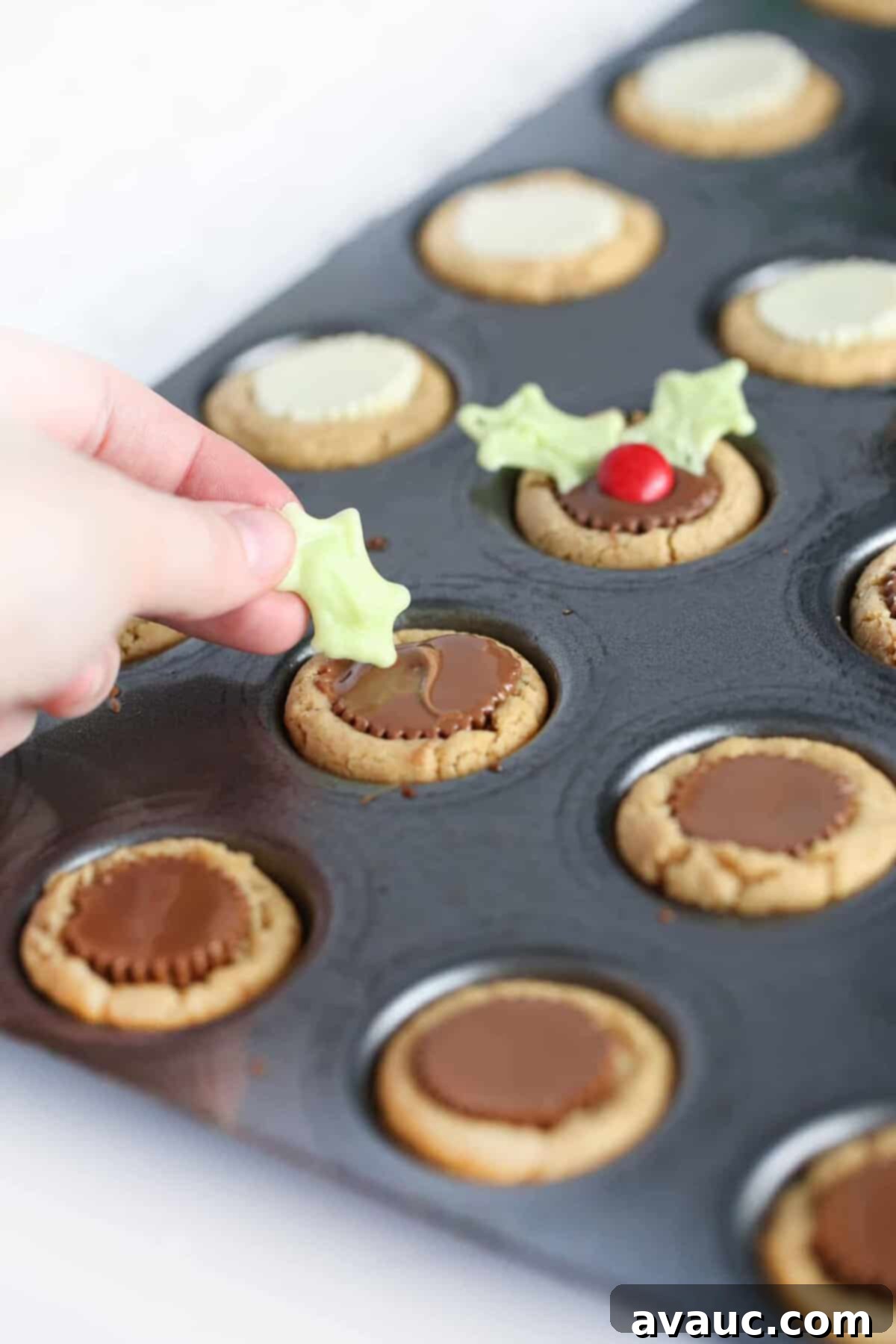 Holly Jolly Cookie Cups 9 Hand placing white chocolate holly leaf into Reeses peanut butter cup cookie to make easy Christmas holly cookie cups.