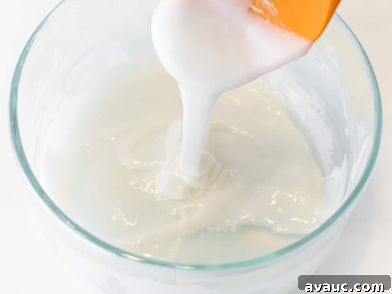 A orange spatula and bowl of whitee cookie icing.