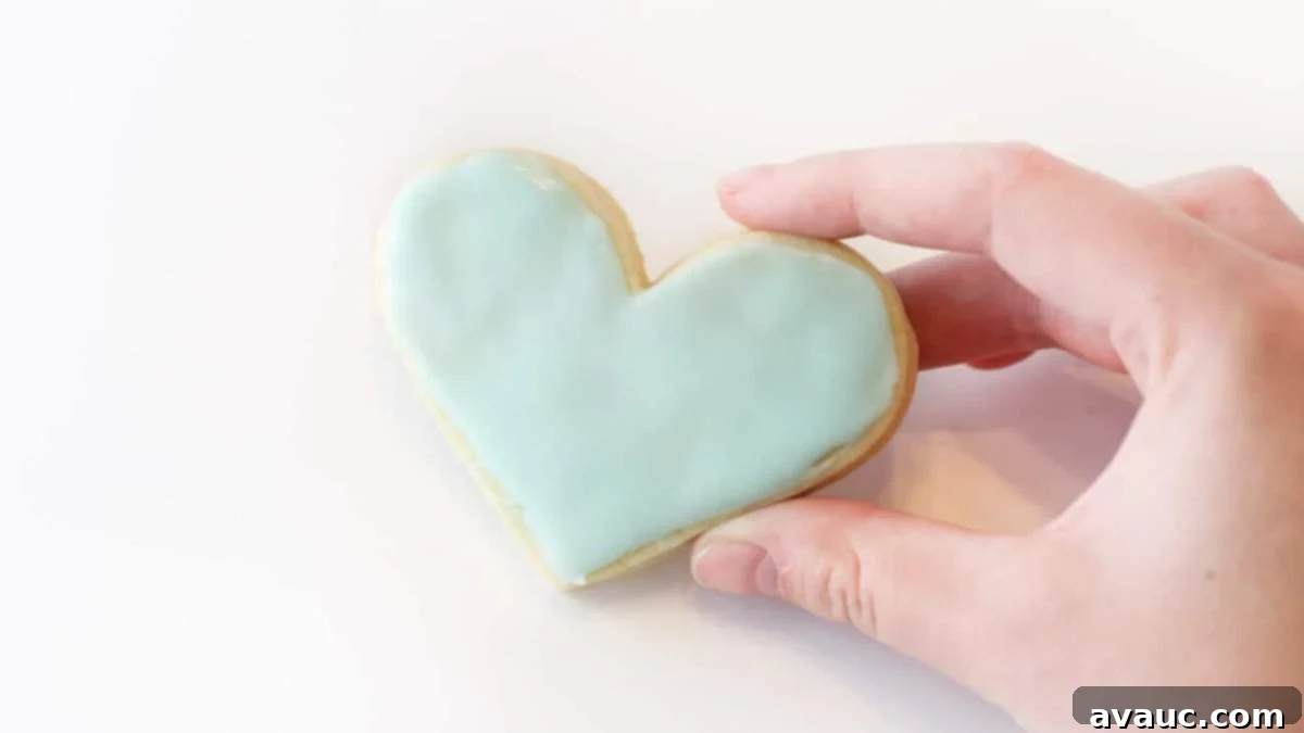 Hand holding blue heart sugar cookie.