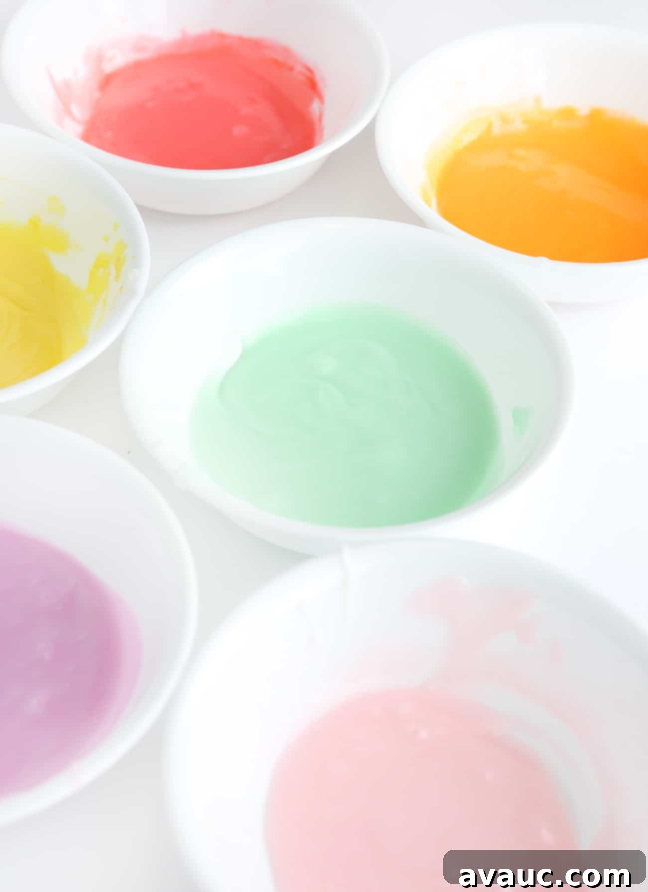 White bowls with different colors of rainbow cookie icing.