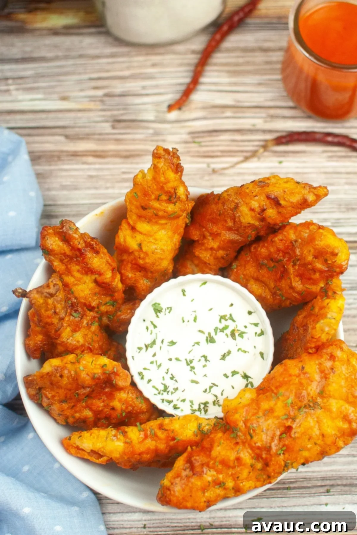 An overhead view of a bowl filled with perfectly golden air-fried chicken tenders and a side of dipping sauce.