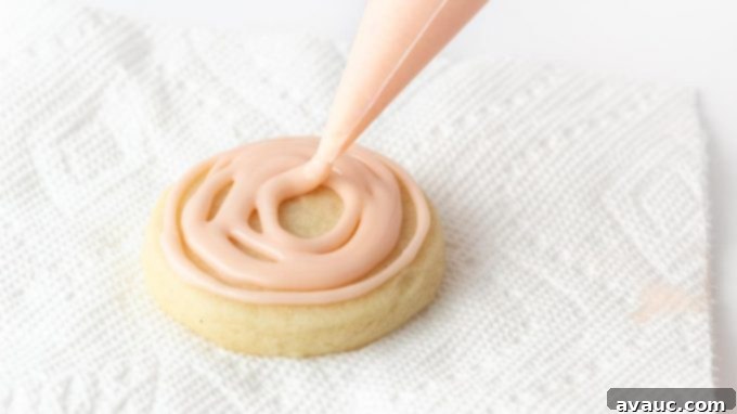 A close-up of beautifully decorated sugar cookies with smooth, pink powdered sugar icing on a cooling rack.