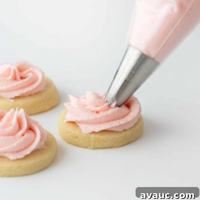 Sugar cookie being piped with swirl pink buttercream frosting
