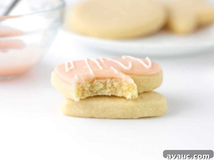 Sugar cookie with a bite taken out, topped with powdered sugar icing for cookies in a light pink hue