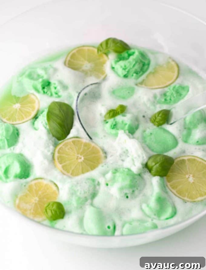 Lime sherbet punch in a bowl, topped with lime slices and basil leaves.