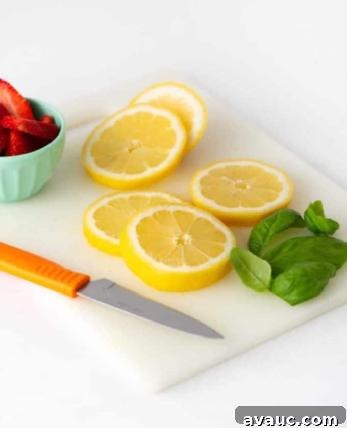 Fresh lemon slices, whole strawberries, and fresh basil leaves on a wooden cutting board, prepared for garnishing.