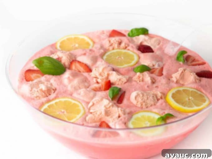 Close-up of a punch bowl filled with Pink Strawberry Sherbet Punch, artfully garnished with floating lemon slices, strawberry slices, and fresh basil.