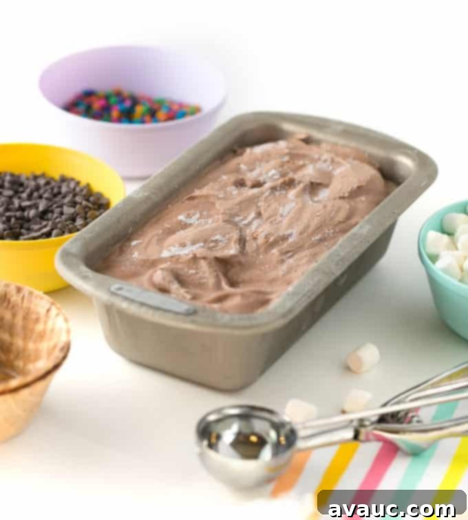 Chocolate no-churn ice cream in a metal loaf pan with various toppings and a scoop ready for serving