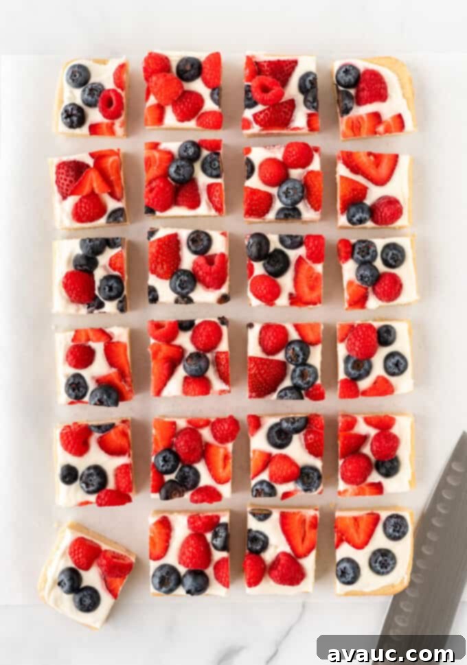 Sugar Cookie Fruit Pizza Bars 2 A large, rectangular sugar cookie fruit pizza topped with cream cheese frosting, sliced strawberries, blueberries, and raspberries.
