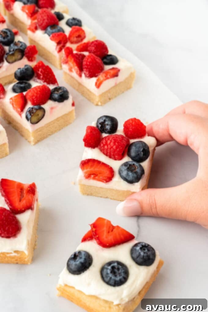 Sugar Cookie Fruit Pizza Bars 12 A stack of beautifully cut sugar cookie fruit pizza bars on a serving plate, showing the thick cookie base, frosting, and berries.