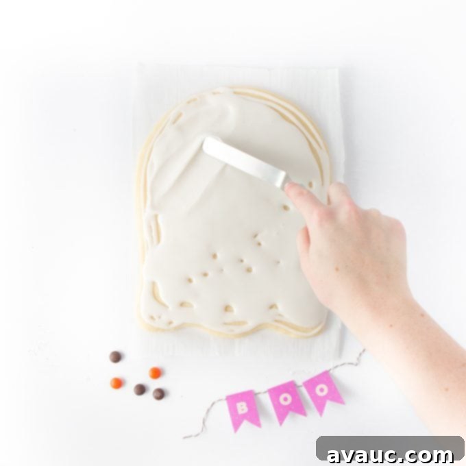 Hand frosting a large ghost sugar cookie cake with white icing for Halloween