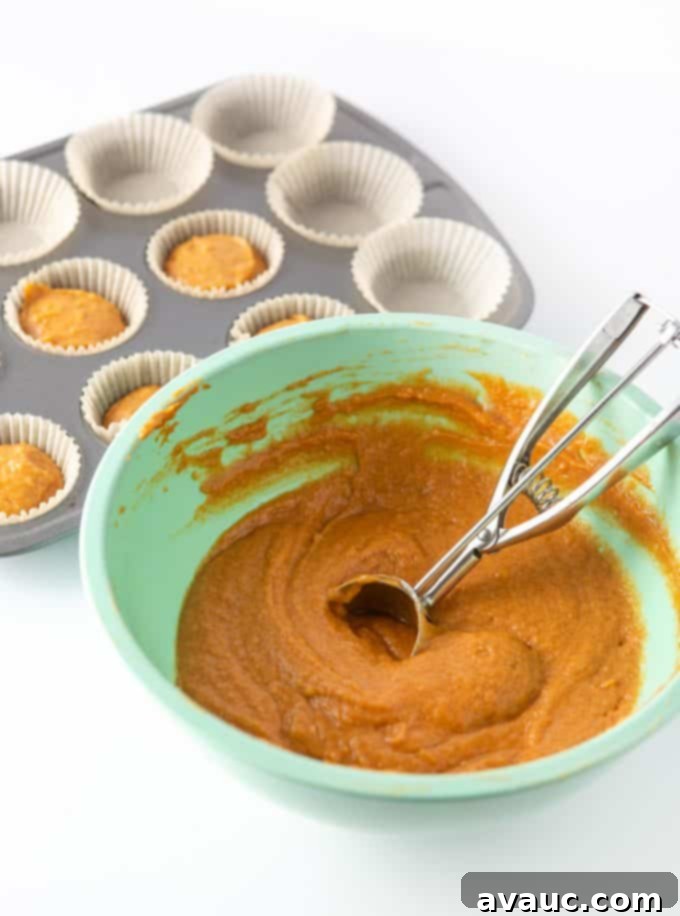Pumpkin cupcake batter scooped into liners in a muffin pan, ready for baking.