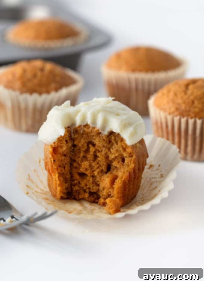 Decorating cooled pumpkin cupcakes with a generous swirl of cream cheese frosting.