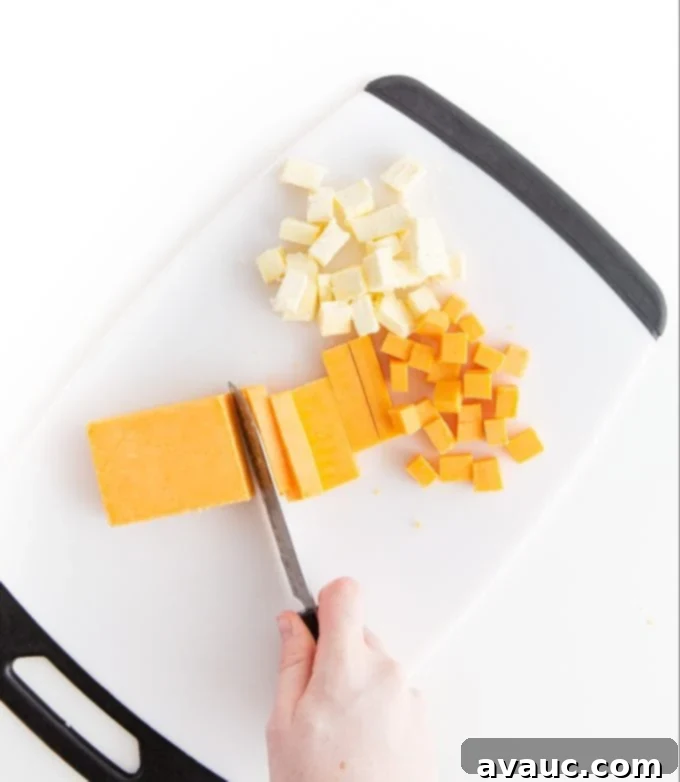 Cutting cheese and butter in small cubes with knife on cutting board to make homemade cheese crackers